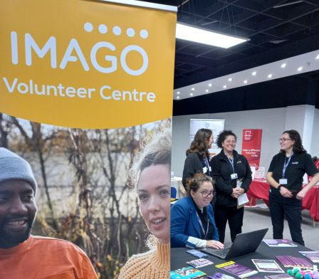Louise from Imago Volunteer centre sitting at a desk next to a display banner with imago volunteer centre written on it